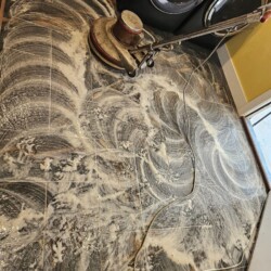 A floor cleaning machine scrubs a tiled floor covered in soapy water in a laundry room.