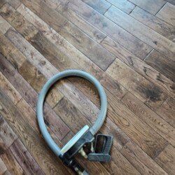 A vacuum hose with a handle attachment lies coiled on a wooden floor.
