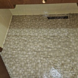 Mosaic tile floor with visible water damage causing warping and discoloration near a wall vent and cabinets.