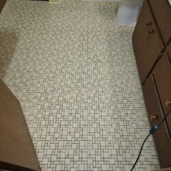 Bathroom with small square and rectangular mosaic tile flooring, wood cabinets, and a white toilet in the background.
