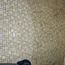 A tiled wall half cleaned by a steam cleaner, showing a stark contrast between clean and dirty sections.